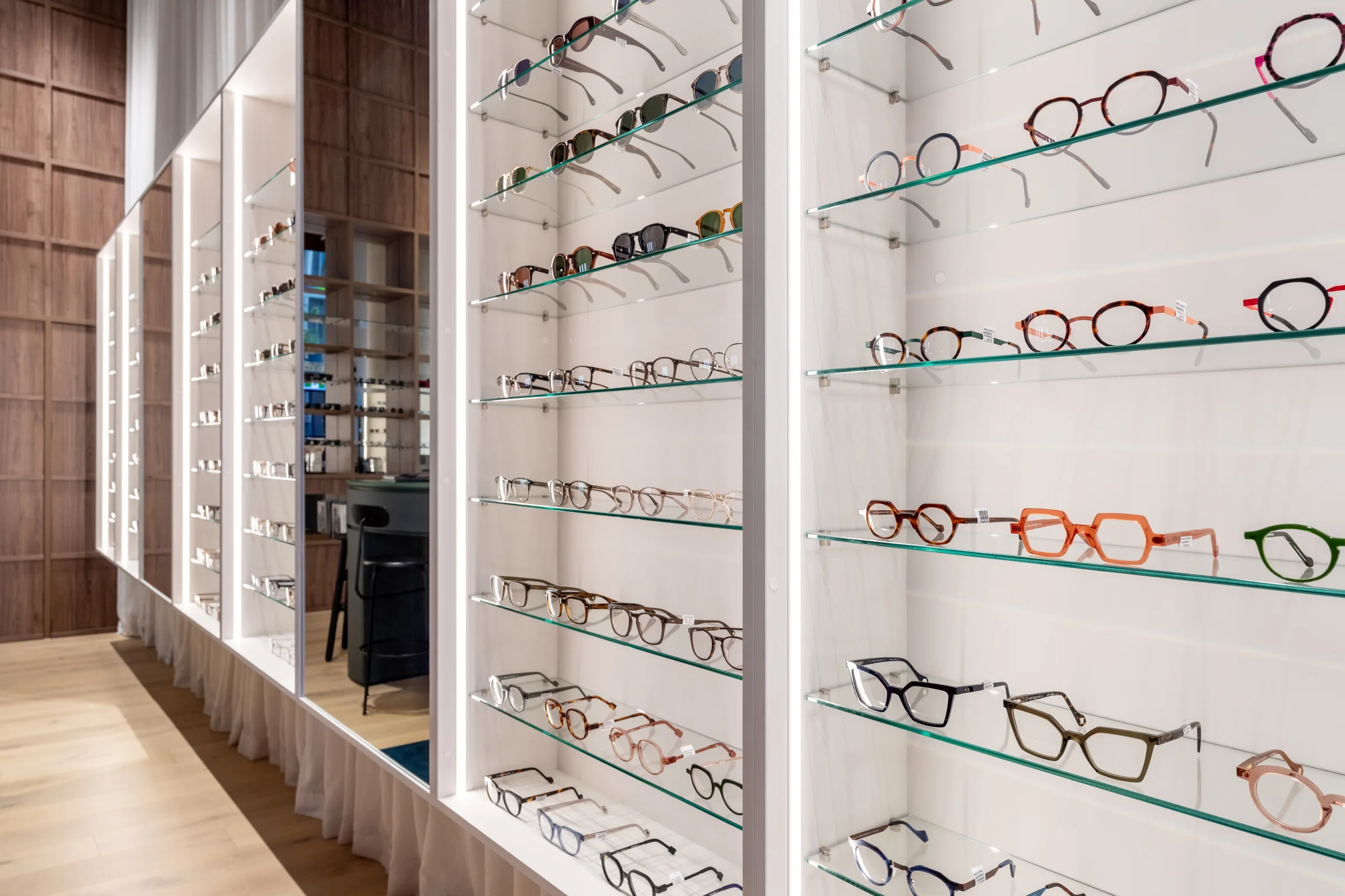 Colour acetate frames on glass shelves in the white shelving at SEASONS Optical.